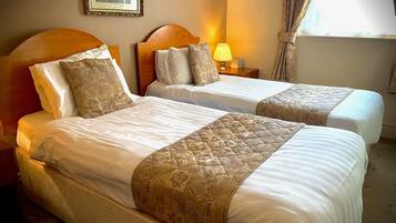 A hotel room with two beds, each with a headboard, a bedside lamp, and a framed picture on the wall.