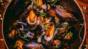 Un bol de moules garni d’herbes et d’oignons, posé sur une surface en bois, illuminé par des guirlandes lumineuses.