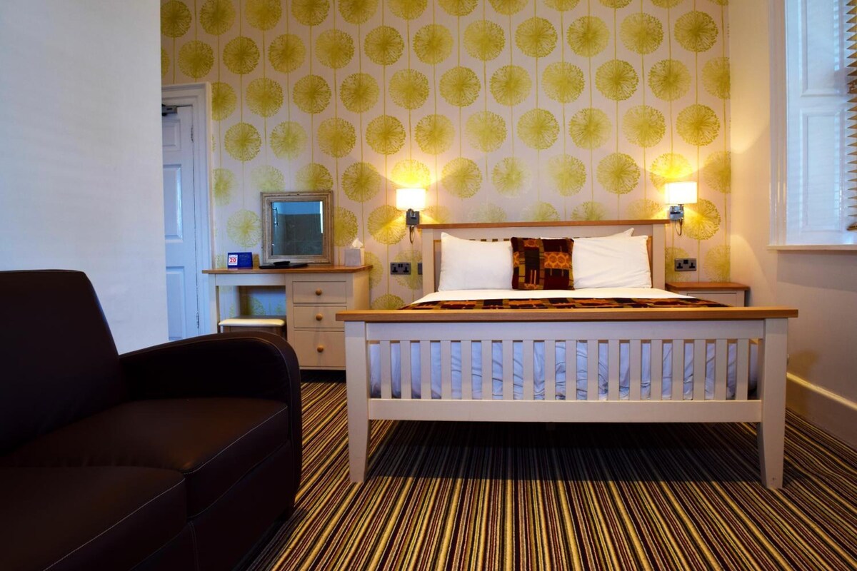 A hotel room with a bed, bedside lamps, a television, and a sofa.