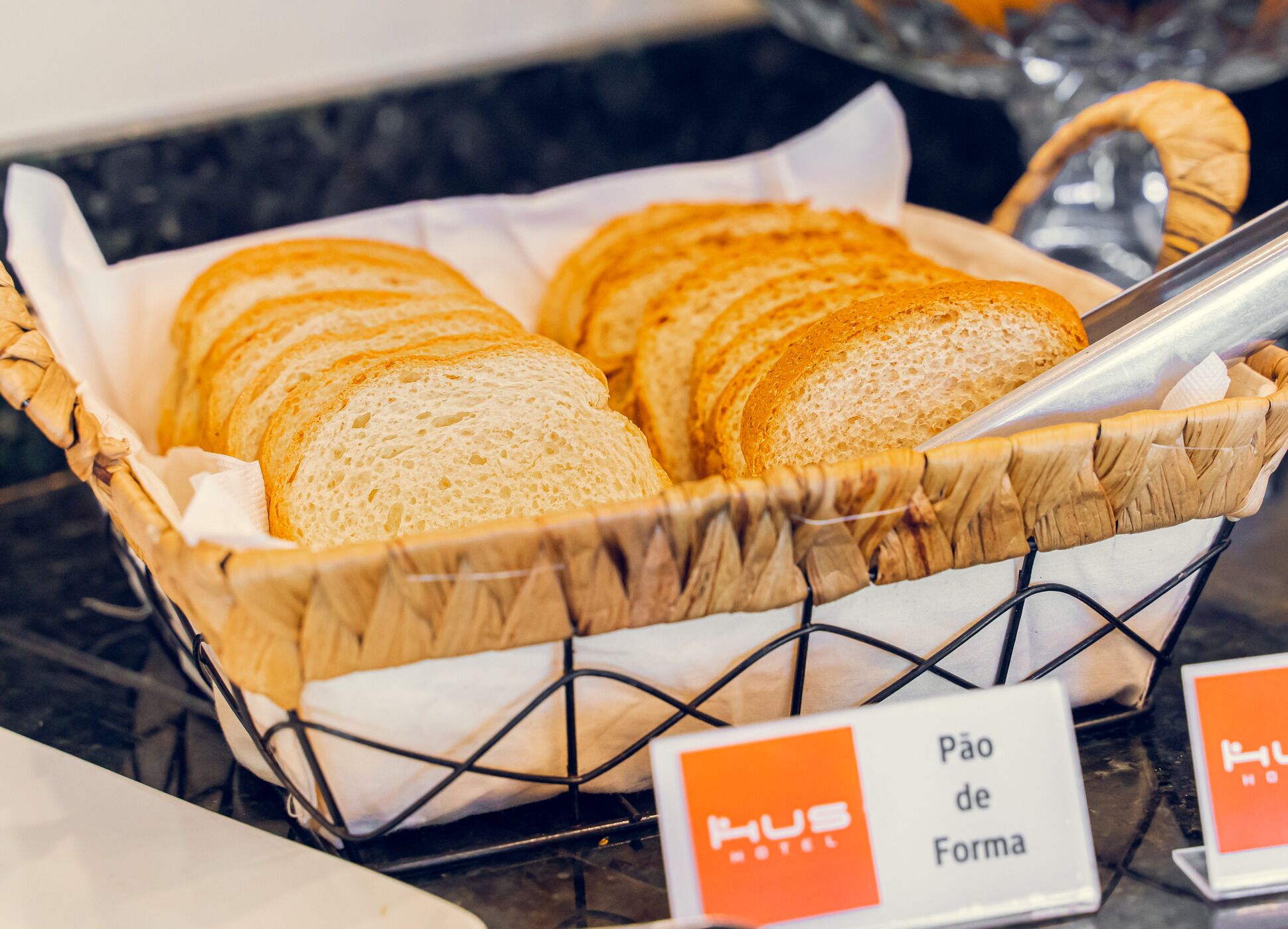 A basket of sliced bread labeled "Pão de Forma" in a hotel setting.