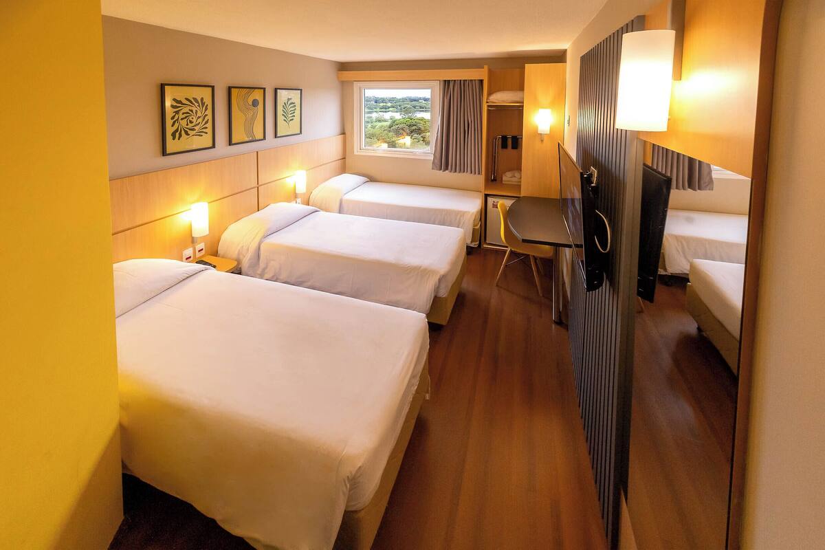 Une chambre d’hôtel avec trois lits simples, un bureau, une chaise et un téléviseur.