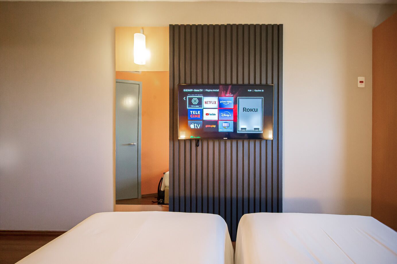 A hotel room with a TV displaying streaming services, a door, and two beds.