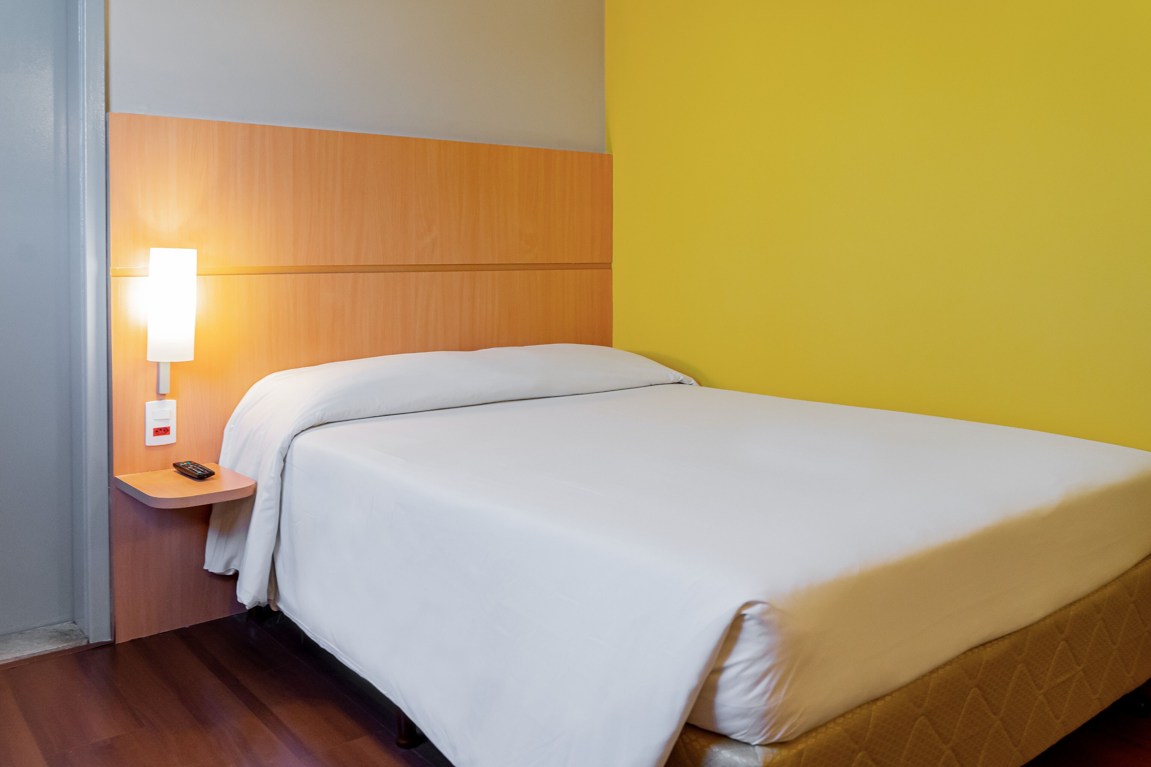 Una habitación de hotel con una cama, una mesita de noche con lámpara y un cabecero de madera.
