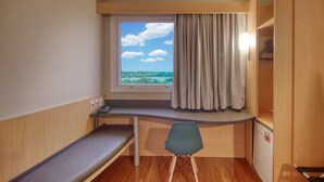 Une petite pièce avec une fenêtre, un bureau, une chaise et un petit lit.