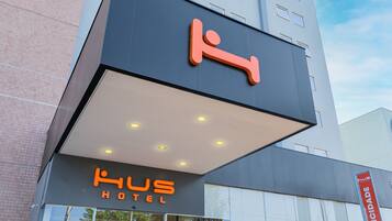 Et hotel med et tydeligt skilt, der viser en stiliseret figur og navnet 'Kus Hotel'.