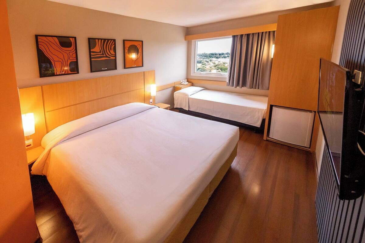 Une chambre d’hôtel avec un grand lit, un plus petit lit, un bureau et une fenêtre avec des rideaux.