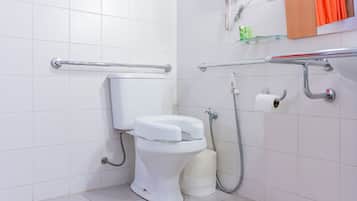 Uma casa de banho moderna com sanita branca, barras de apoio, chuveiro e suporte para papel higiénico.