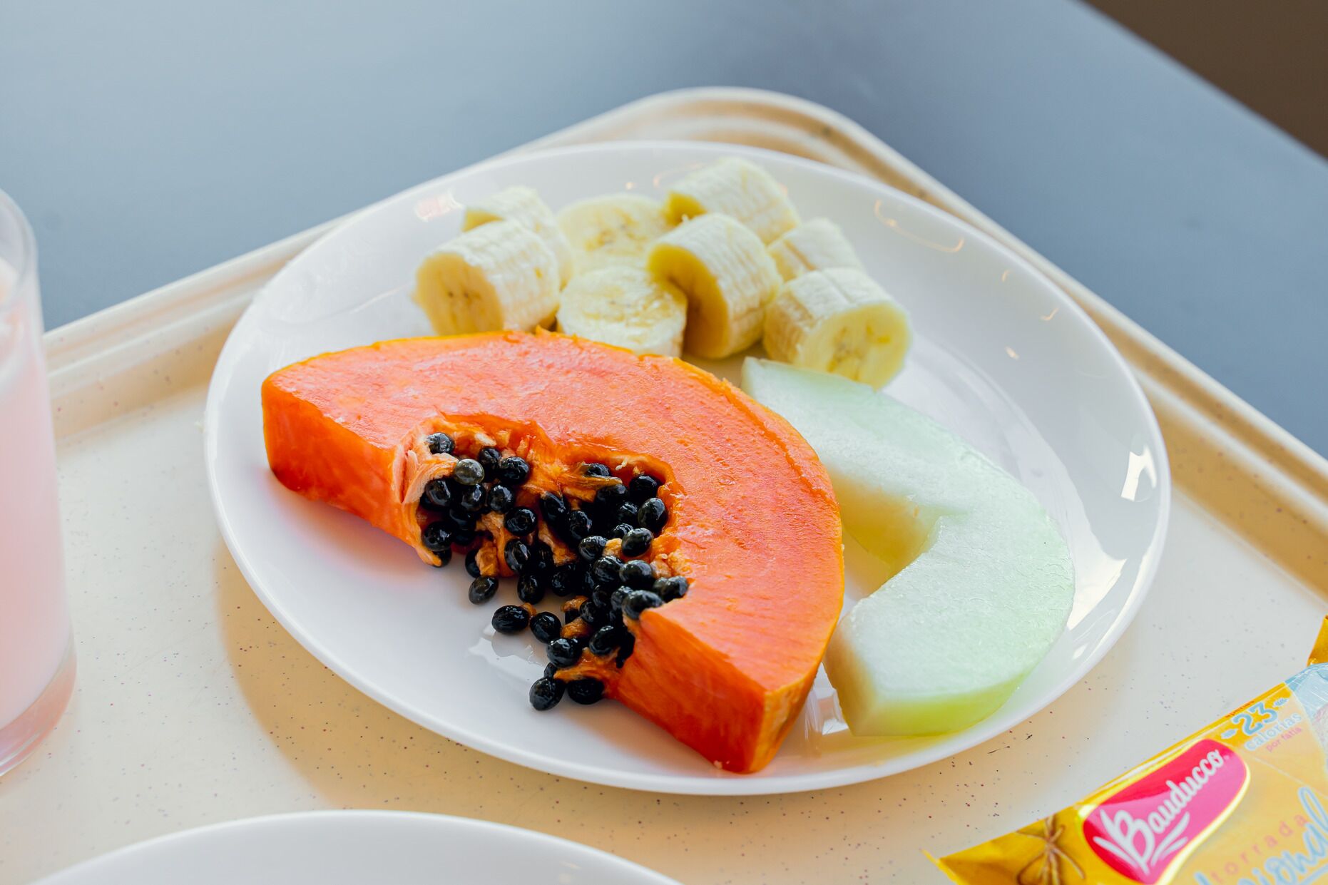 A plate with a slice of papaya, banana slices, and a melon on a tray.