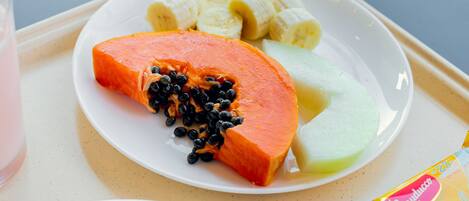 A plate with a slice of papaya, banana slices, and a melon on a tray.