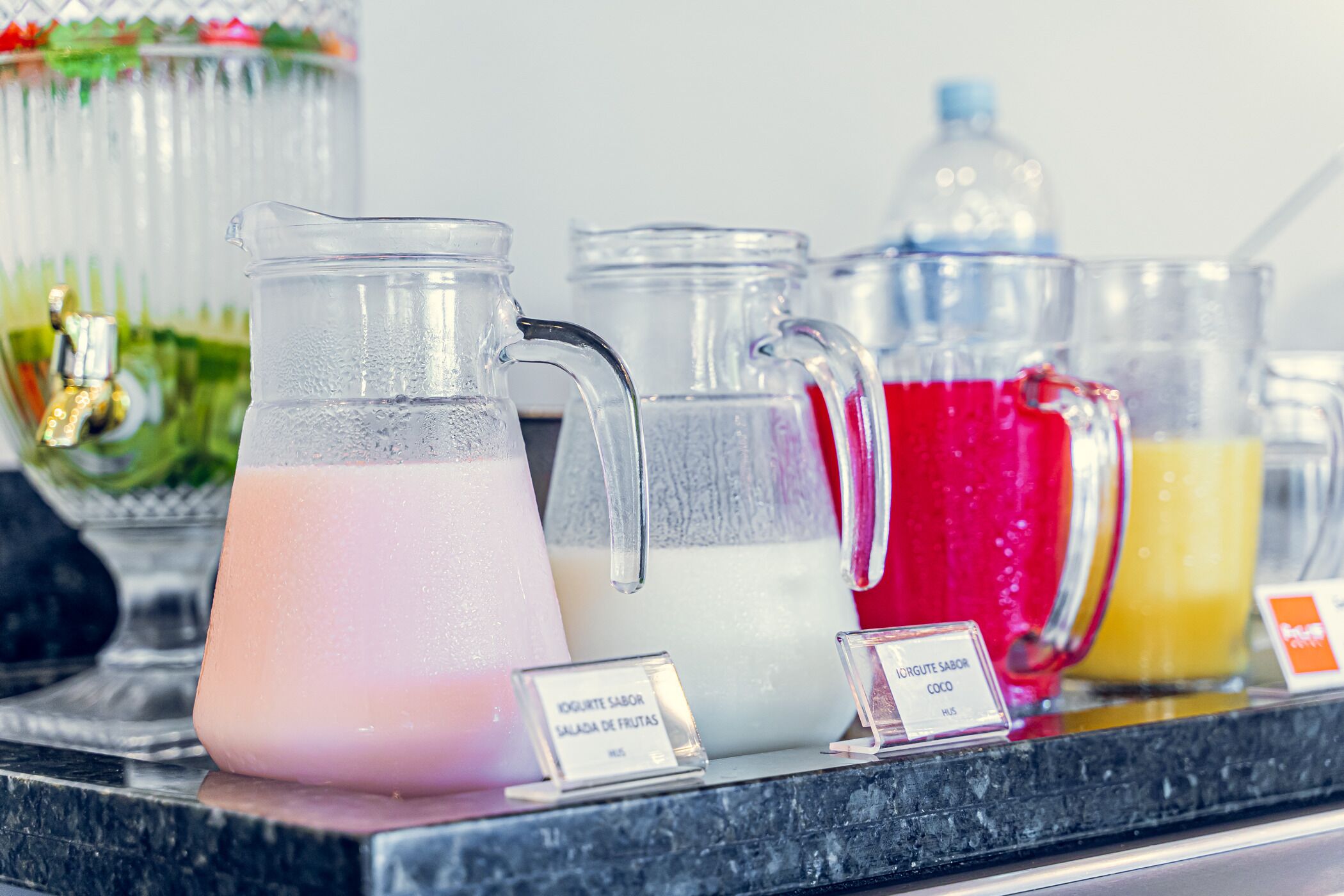 A variety of beverage dispensers on a counter, including a pitcher of pink drink, a pitcher of white drink, and a pitcher of red drink.