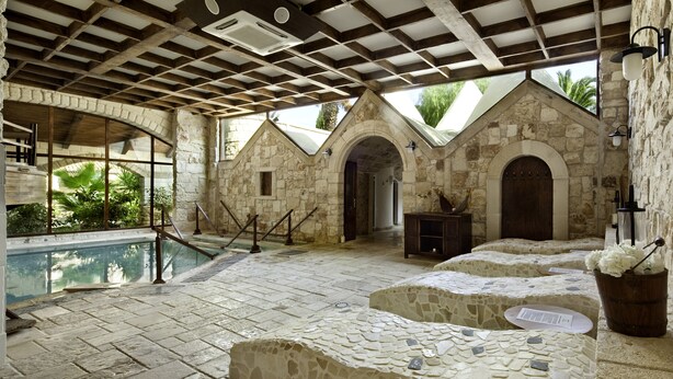 Zona de piscina con paredes de piedra, un banco de piedra, un cubo de madera con flores y vistas a la vegetación.