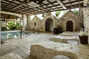 A stone-walled pool area with a stone bench, a wooden bucket with flowers, and a view of greenery outside. - UNAHOTELS Regina Bari (Noicattaro)