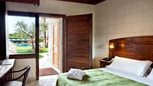 Habitación de hotel con cabecera de madera, cama con colcha verde, mesita de noche con lámpara y vistas a una zona de piscina al aire libre.