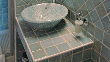 A bathroom with a large, round, blue-tiled sink, a mirror, and a soap dispenser.
