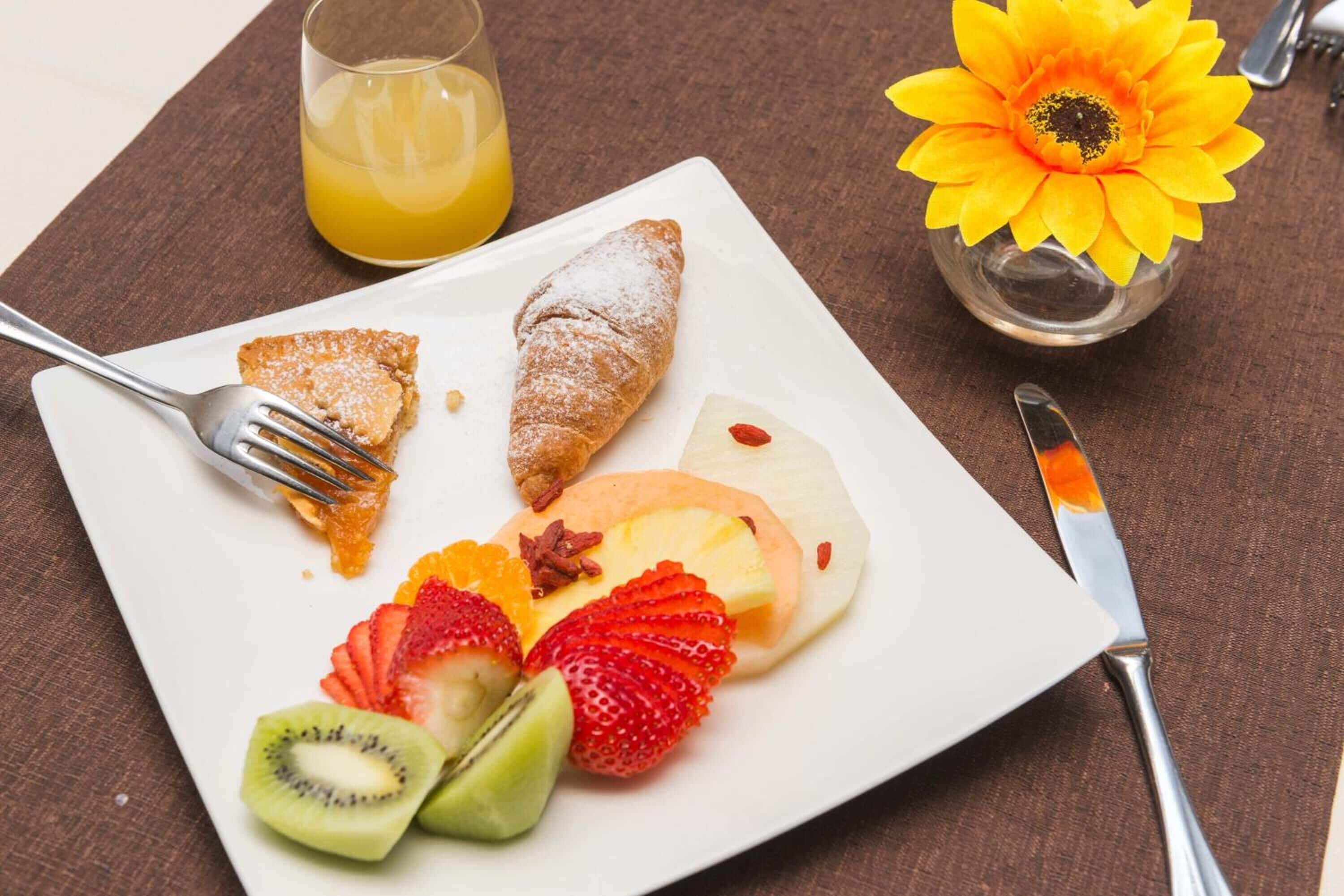 Ein Frühstücksteller mit einem Croissant, Fruchtscheiben und einem Glas Orangensaft.