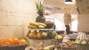 Una exhibición de frutas con plátanos, piña, naranjas, peras y manzanas en cestas.