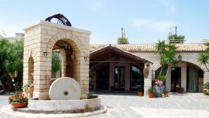 Un patio con una fuente de piedra, un edificio con arcos y plantas en macetas.