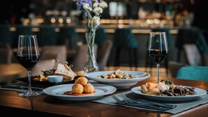 Une table à manger avec des assiettes remplies de nourriture, des verres de vin rouge et un vase de fleurs.