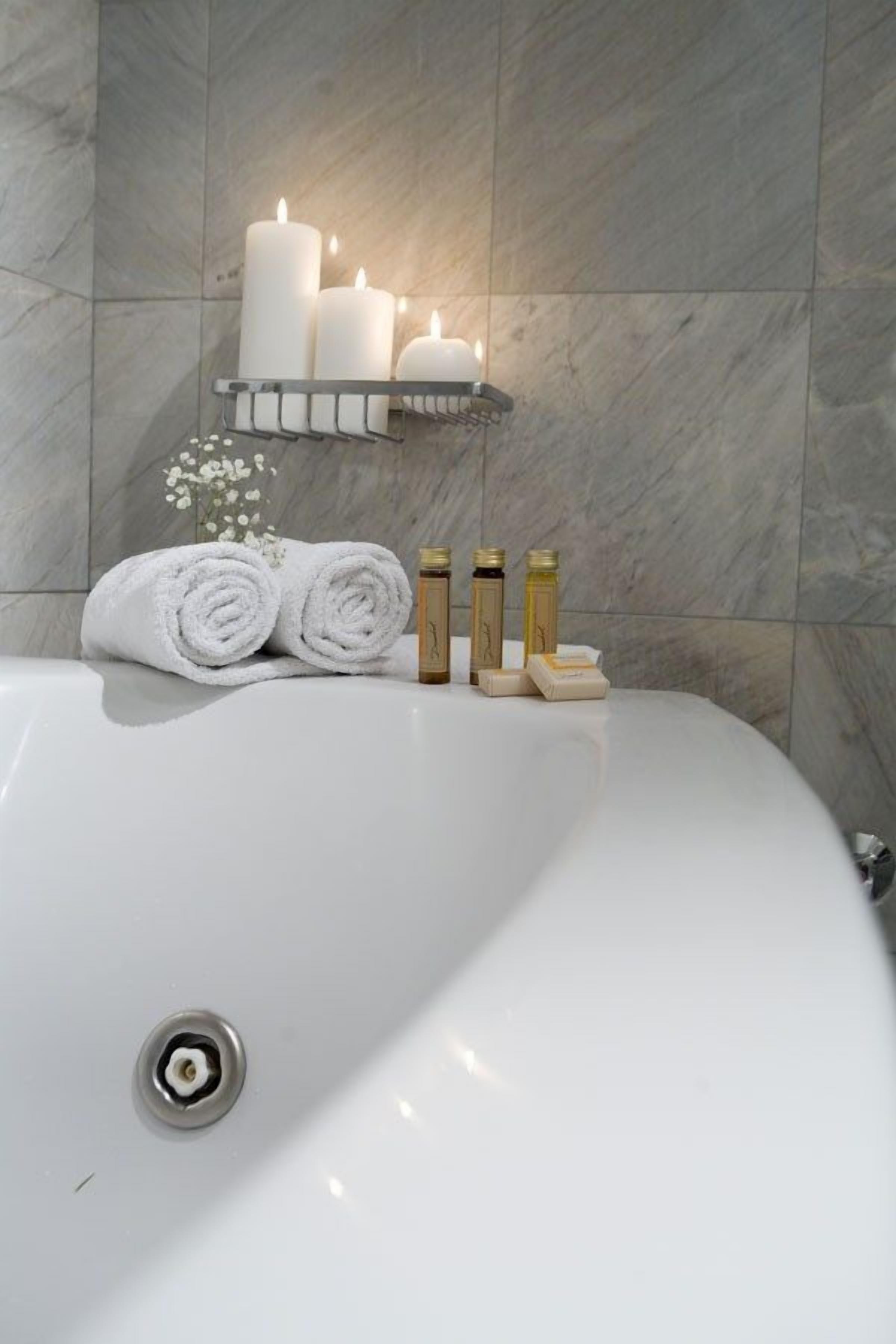 Un baño con una bañera blanca, una repisa con velas, toallas dobladas y artículos de aseo.