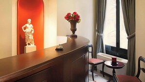 Un hall d’hôtel avec un comptoir d’accueil incurvé, une statue, un vase de fleurs et une fenêtre avec des rideaux.