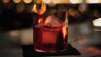 A glass of red beverage with ice cubes and a decorative garnish on a black coaster.