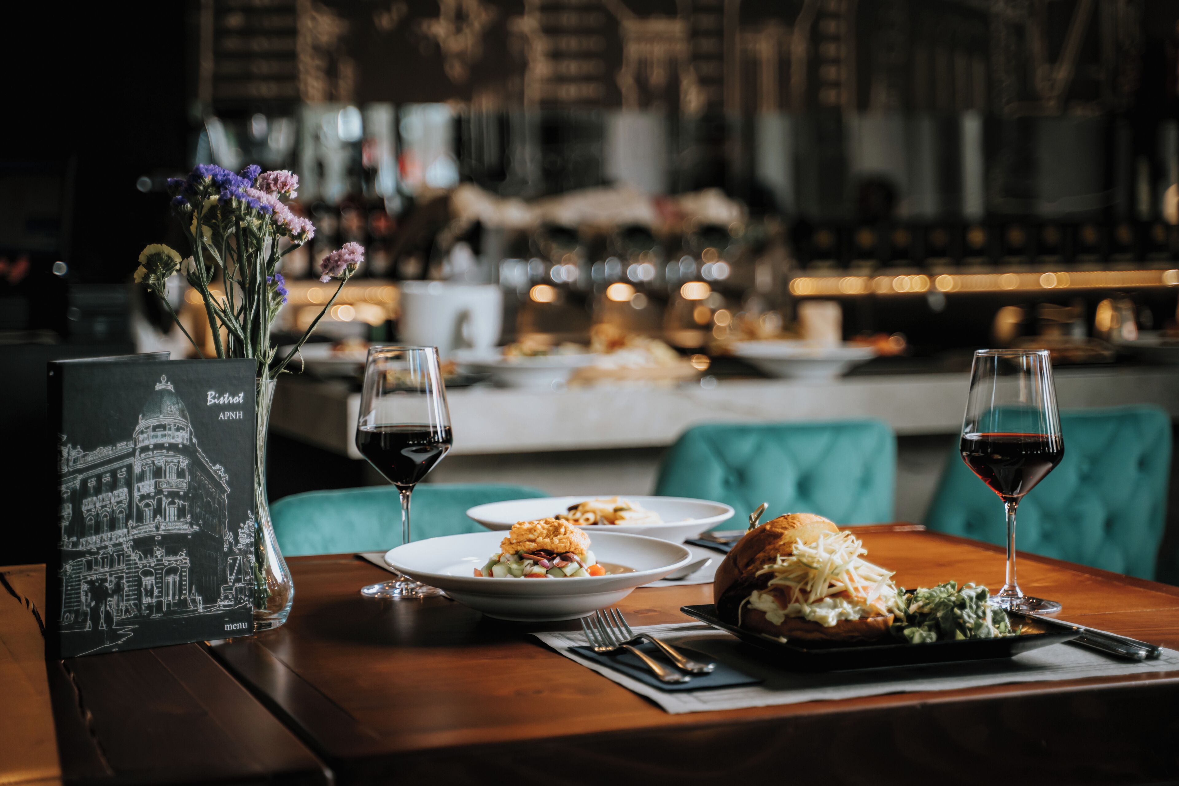 En restaurantscene med et bord dækket til to personer, inklusive en menu, to vinglas og tallerkener med mad.
