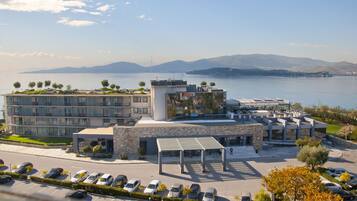A modern hotel with a parking lot, a covered outdoor area, and a view of a lake and mountains.