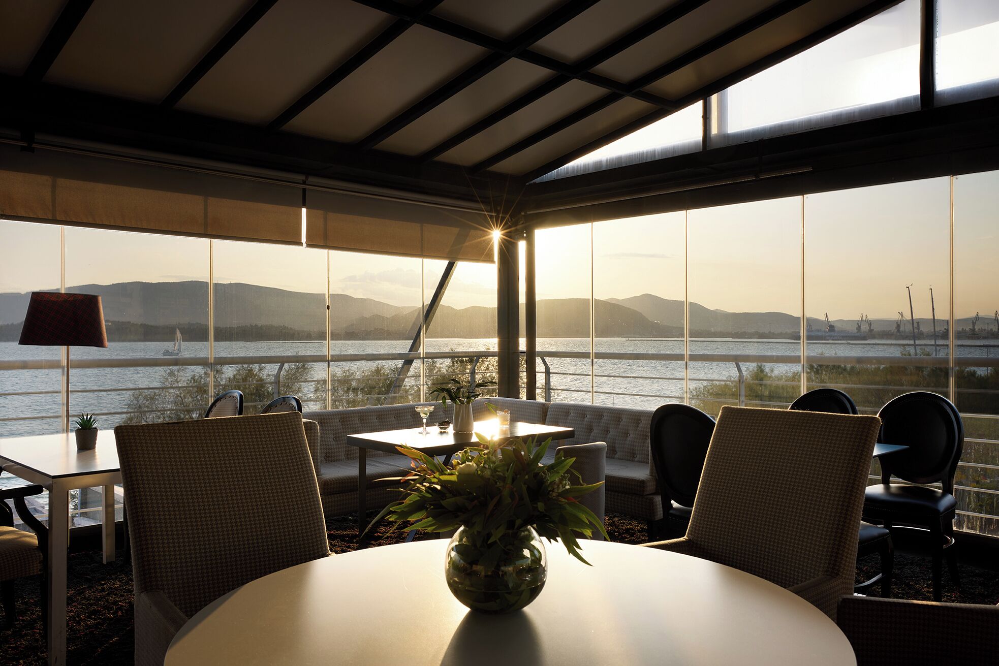 Un comedor con mesa y sillas, una planta en maceta y vistas a una masa de agua y montañas lejanas.