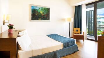 Une chambre d’hôtel avec un lit, un bureau doté d’une lampe, une chaise, un tableau au mur et un balcon avec vue.