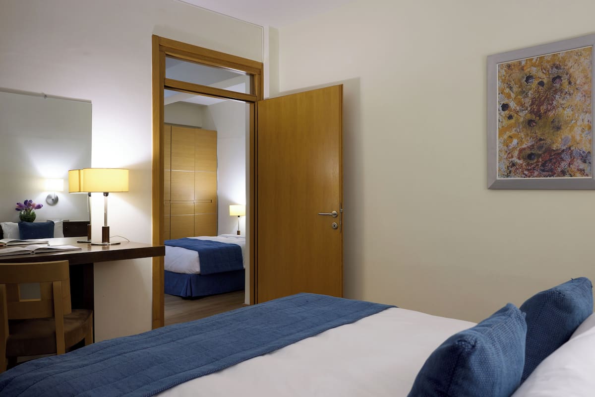 A hotel room with a bed, desk, chair, and a door leading to another room.