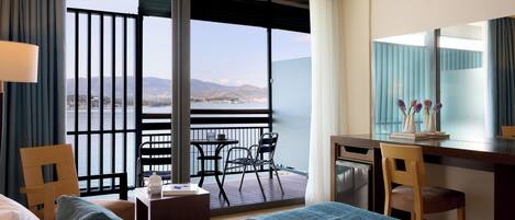 Habitación de hotel con cama, escritorio, silla, mesita y vista al mar.