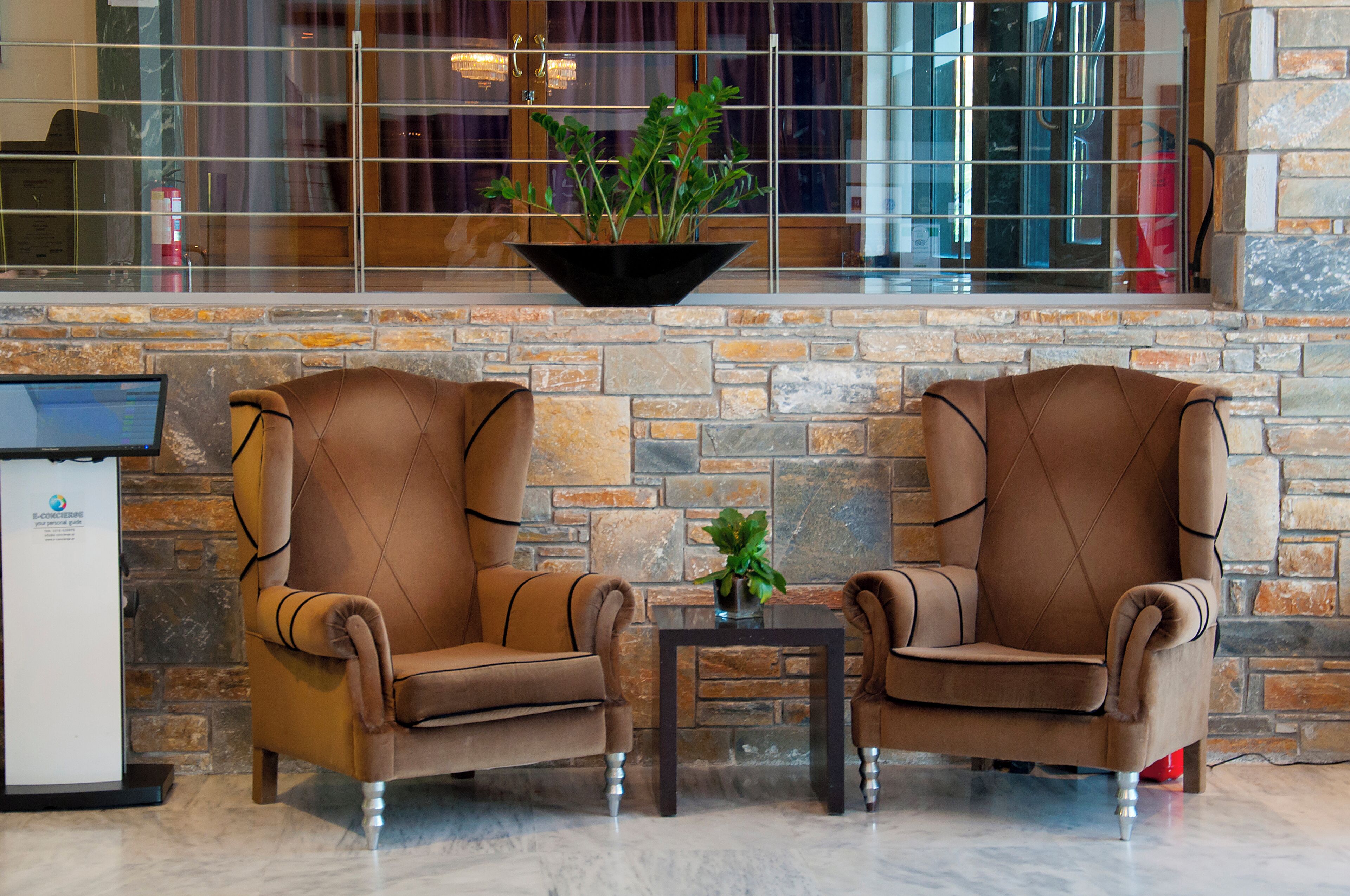 A lobby with two brown leather armchairs, a small table with a plant, and a stone wall.