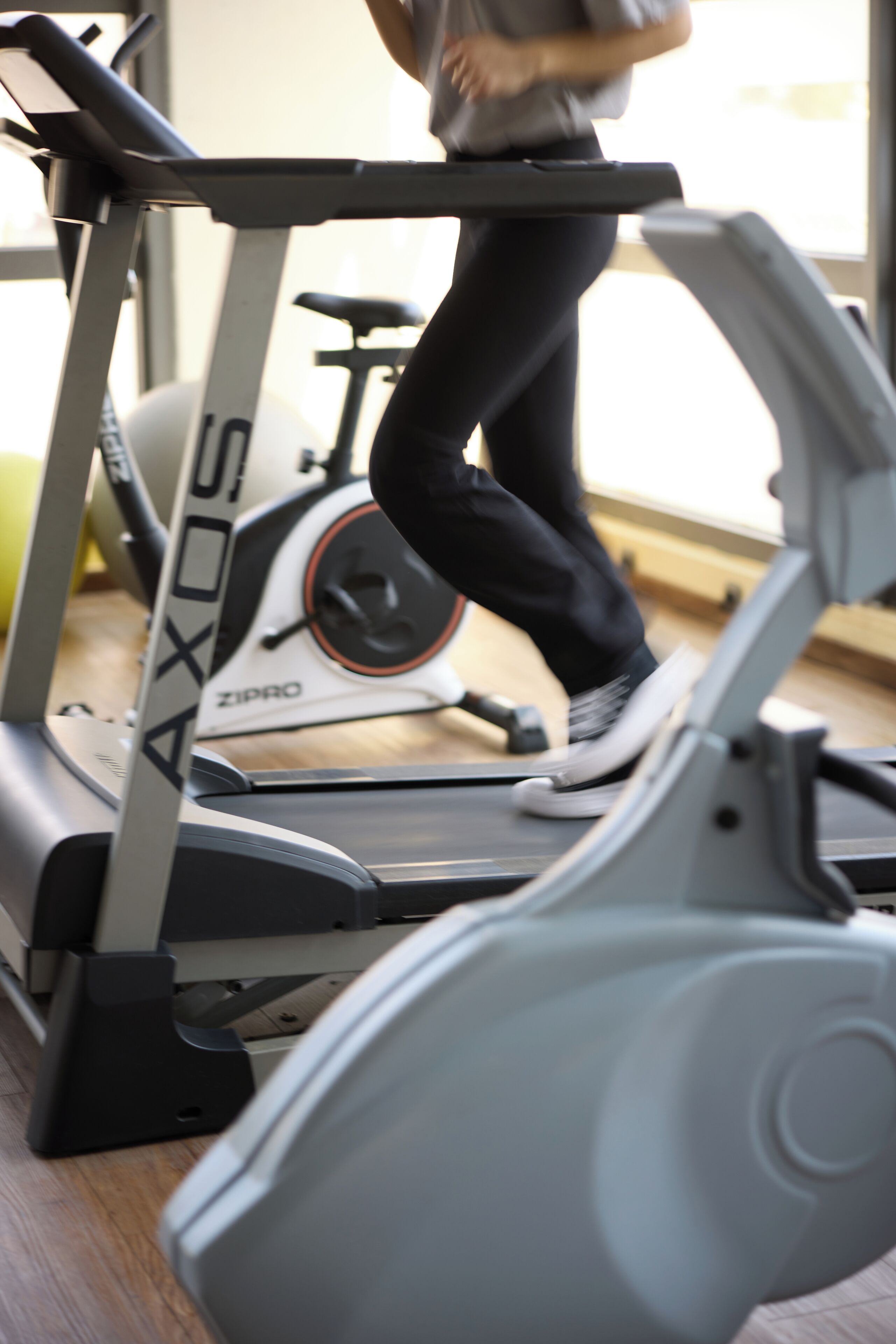 A treadmill with a person using it, a stationary bike, and a yellow exercise ball in the background.