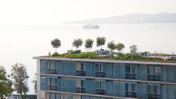 A multi-story building with balconies, a rooftop garden with trees, and a view of a body of water with a ship in the distance.
