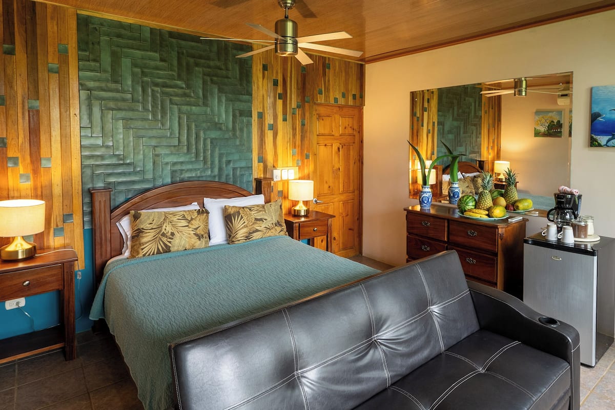 Une chambre d’hôtel avec un lit, un canapé, un bureau avec un ordinateur, un miroir et un tableau au mur.