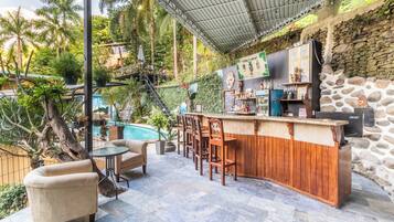 An outdoor bar area with a pool, wooden bar counter, and seating.