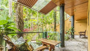 Une terrasse couverte avec une table en bois, une chaise rembourrée et un banc.