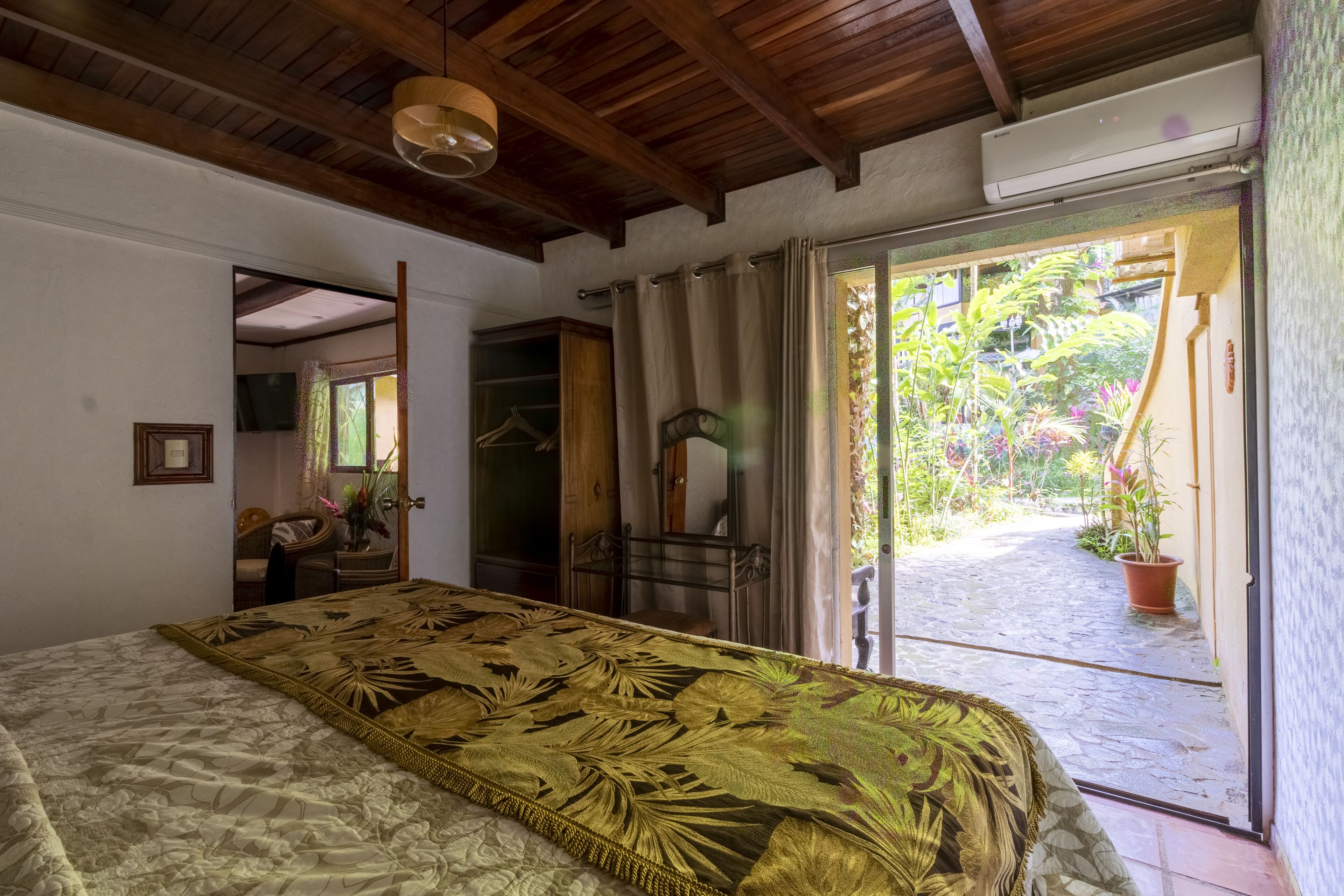 A bedroom with a bed, a wooden ceiling, a sliding glass door leading to a garden.