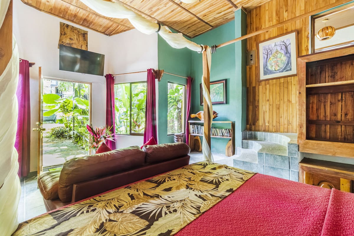 Une chambre dotée d’un grand lit, d’un canapé, d’une télévision, d’une bibliothèque et offrant une vue sur la verdure environnante.