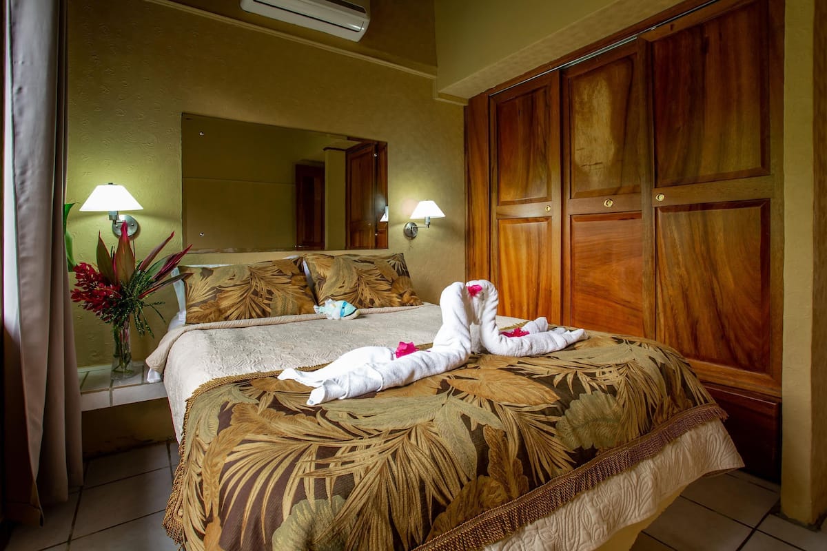 Une chambre d’hôtel avec un lit, un grand miroir, une armoire en bois et deux lampes fixées au mur.