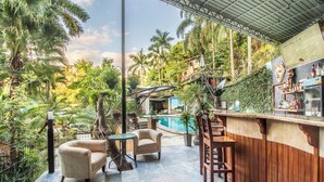 Un espace bar avec des meubles en bois, une piscine et une végétation luxuriante.