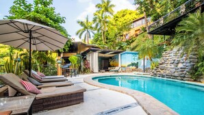 Un espace aménagé au bord de la piscine, avec des chaises longues, un parasol et un mur en pierre.