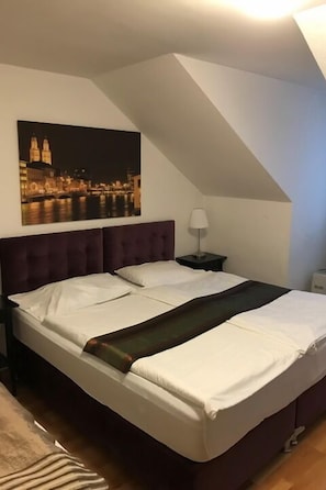 Un dormitorio con una cama grande, una mesita de noche, una lámpara y un cuadro de un paisaje urbano en la pared.