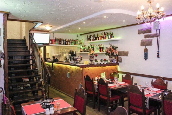A restaurant with a bar area, wooden chairs, and a staircase leading to another level.