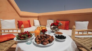 Mesa de comedor con comida y bebidas en una terraza con cielo despejado.