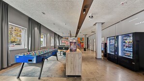 Amplio espacio interior con mesa de fútbol de mesa, máquinas expendedoras y vistas al exterior a través de grandes ventanales.