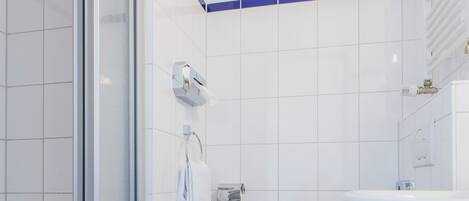 Et moderne badeværelse med en glasbrusekabine, et hvidt toilet og en vask.
