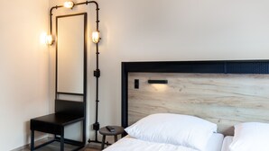 Habitación de hotel con un espejo grande, cabecera de madera y una mesita con control remoto.