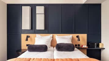 Ein Doppelbett mit zwei Kissen, ein Nachttisch mit Lampe und ein an der Wand befestigter Flachbildfernseher.