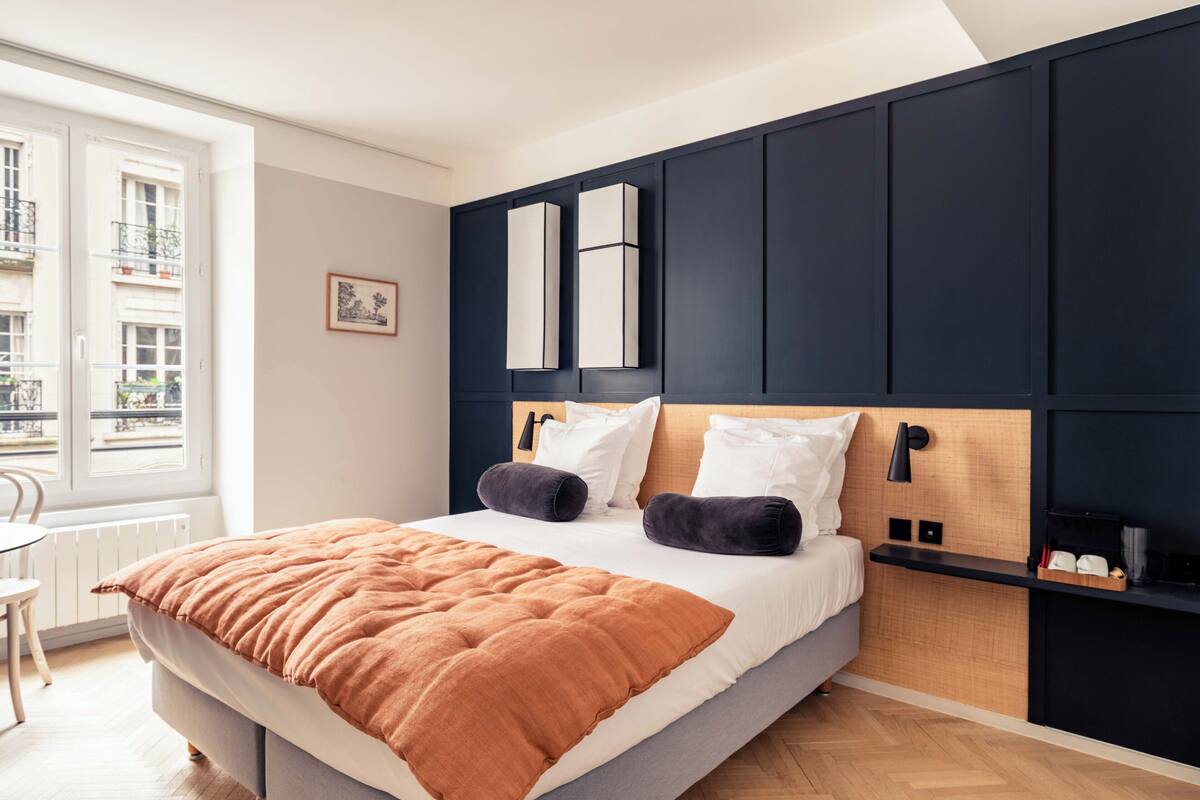 Ein modernes Schlafzimmer mit Bett, Nachttisch, Fenster und Blick auf Gebäude.